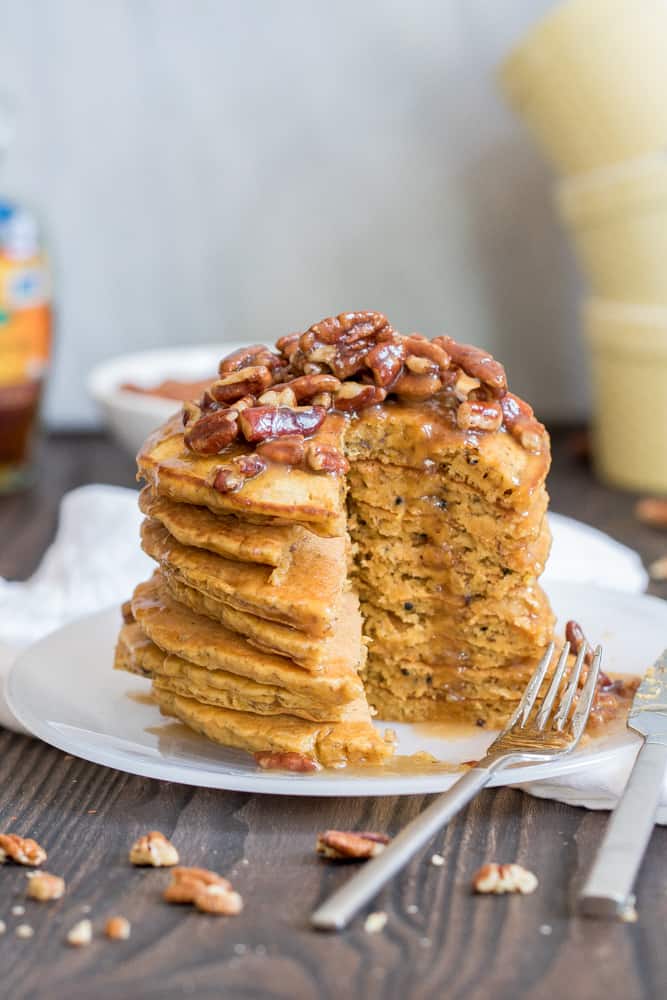 Stack of Pumpkin Quinoa Pancakes with Praline Syrup missing a slice on a plate with a fork.