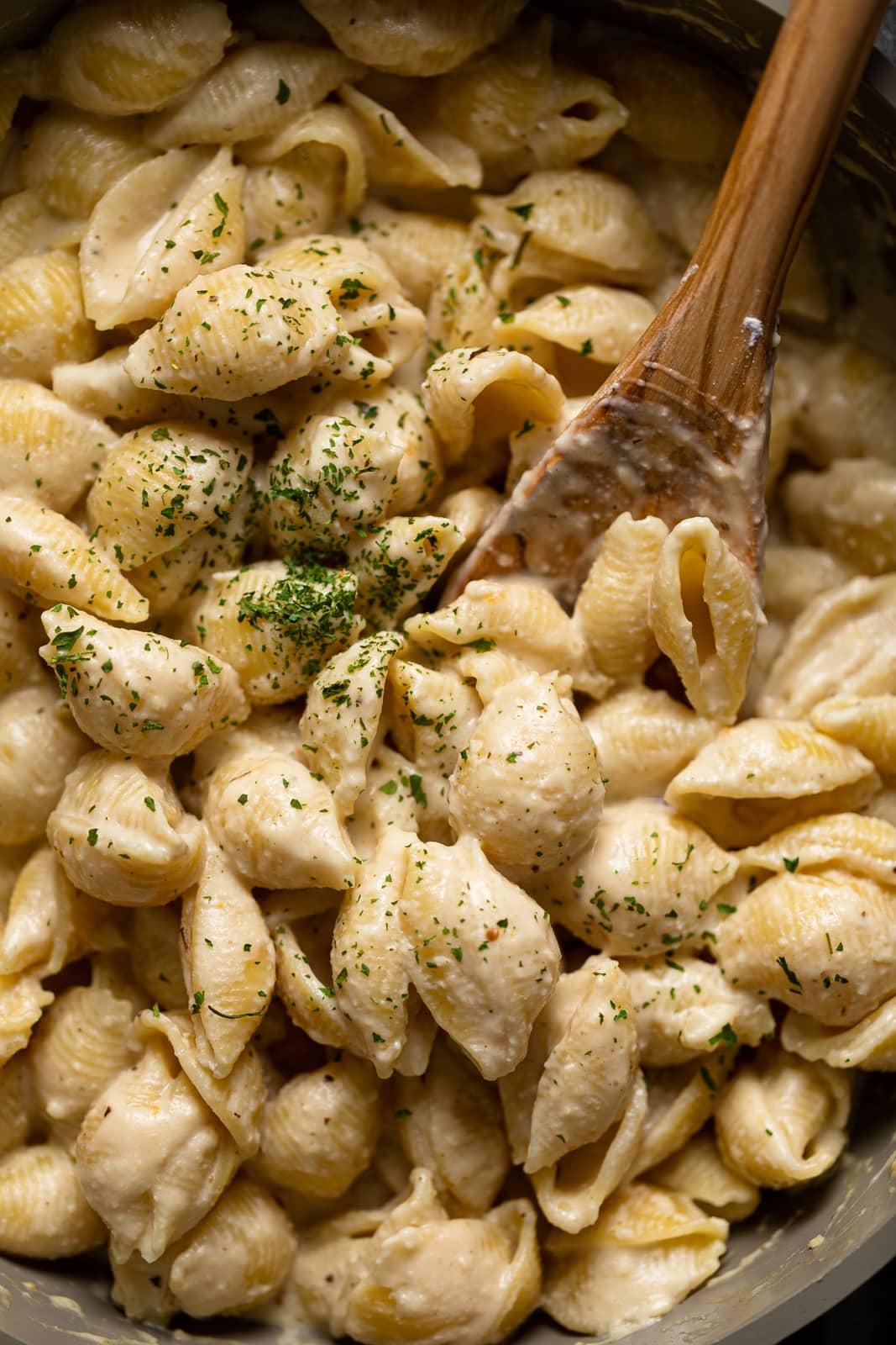 Closeup of a wooden spoon stirring Vegan Mac and Cheese