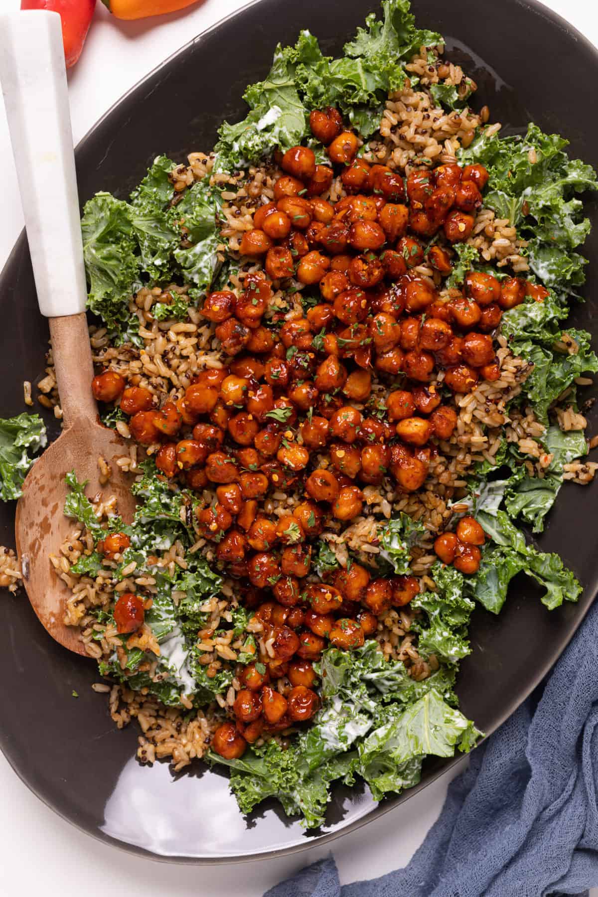 Wooden spoon stirring Loaded Kale Salad with Spicy Chickpeas