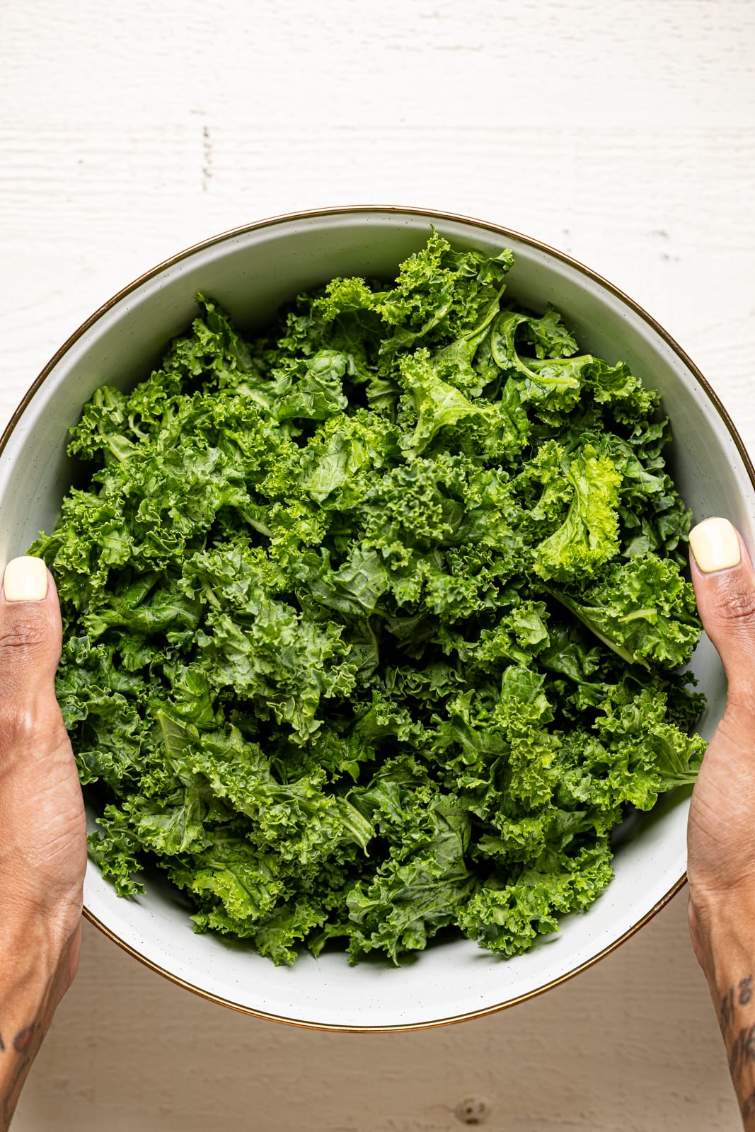 Fresh kale leaves in a white bowl on a white wood table.