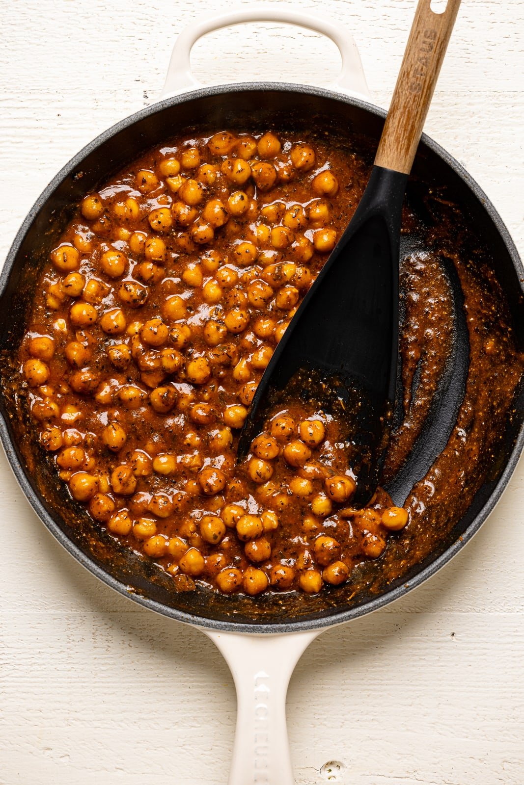 Cooked buffalo chickpeas in a white skillet on a white wood table. 