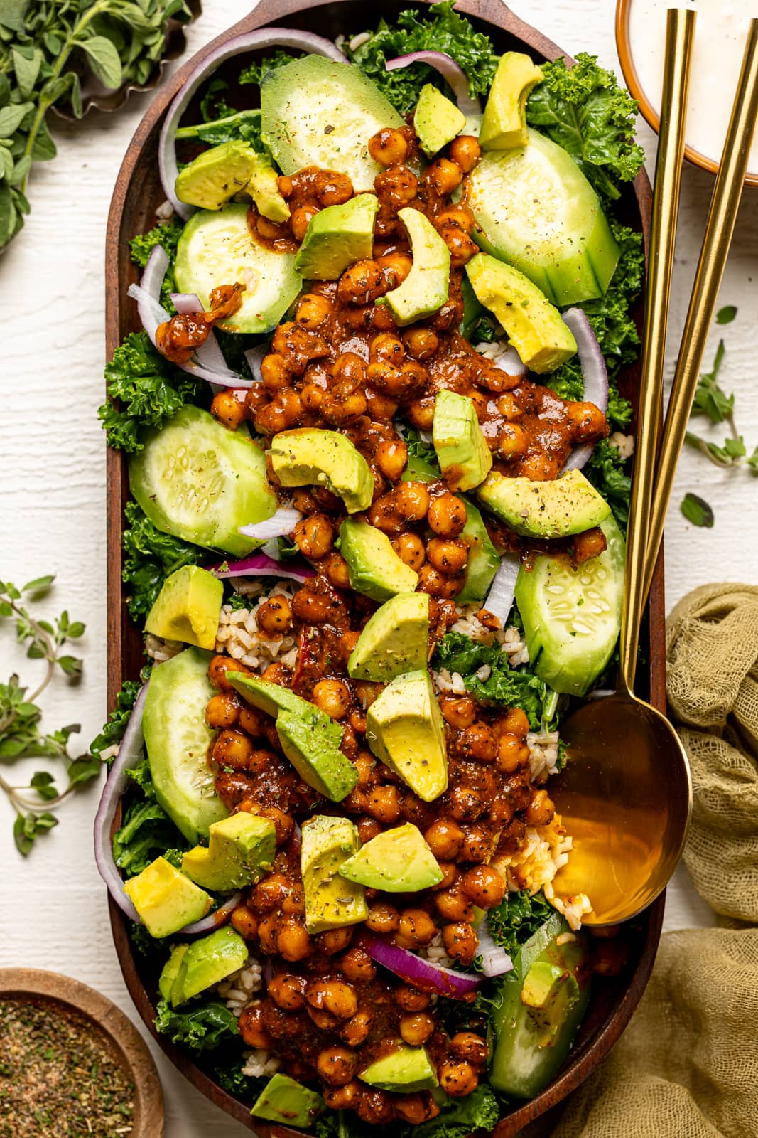 Kale salad in a large wooden serving dish with two gold spoons.