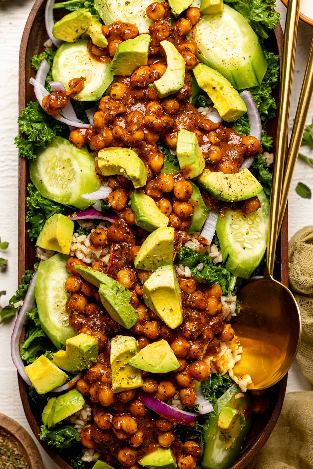 Kale salad in a large wooden serving dish with two gold spoons.