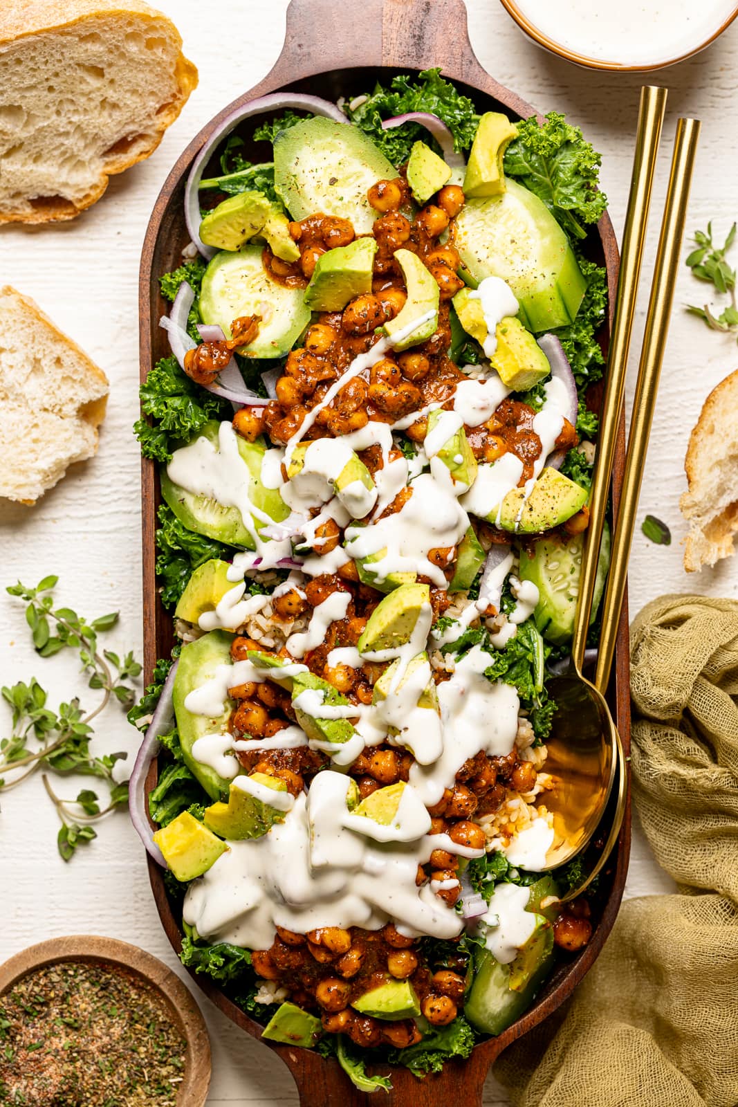 Fully loaded Kale salad with white dressing in a large wooden serving dish with two gold spoons.