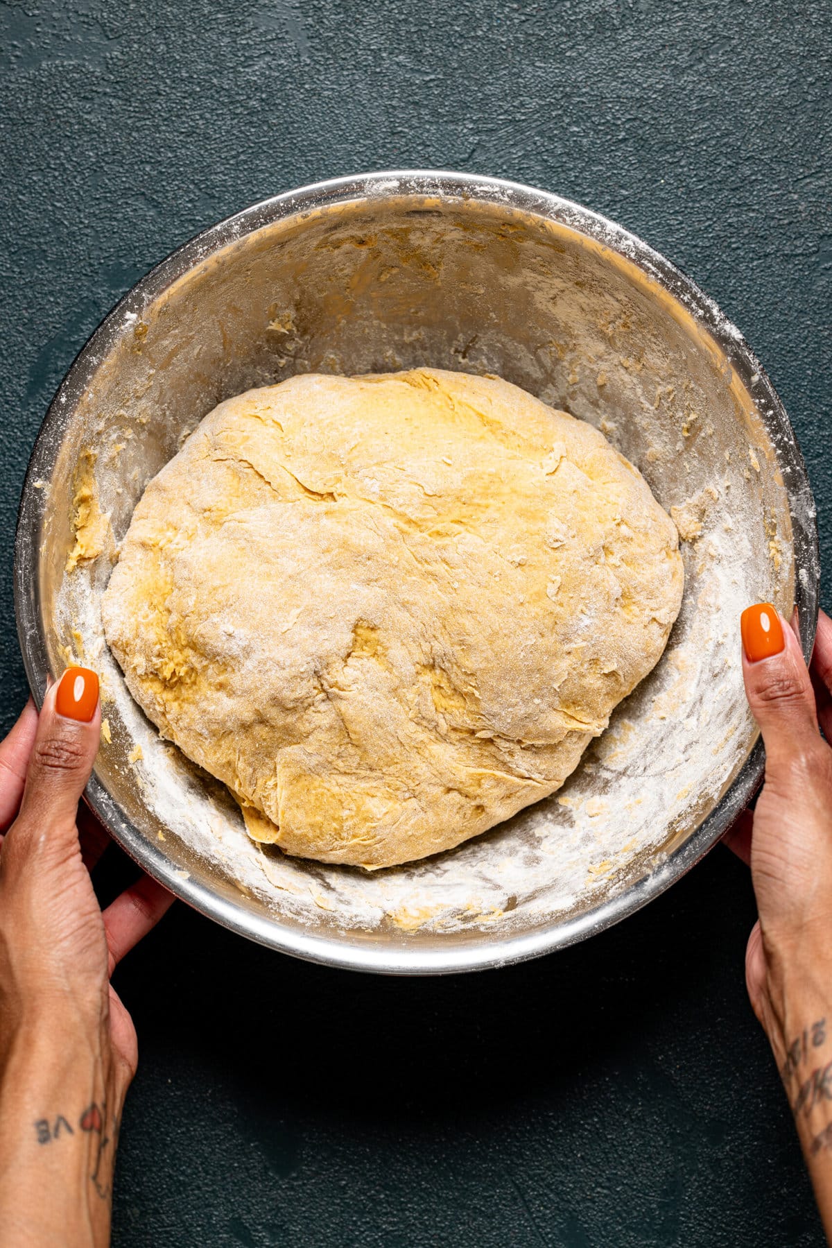 Dough in a silver bowl being held. 