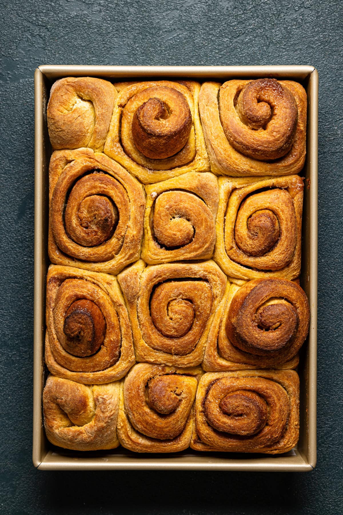 Baked golden brown cinnamon rolls in a baking dish.