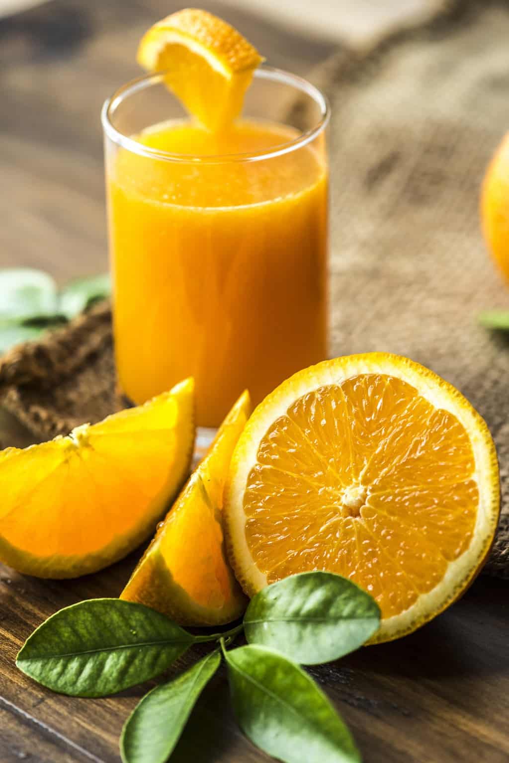 Oranges next to a glass of orange juice.