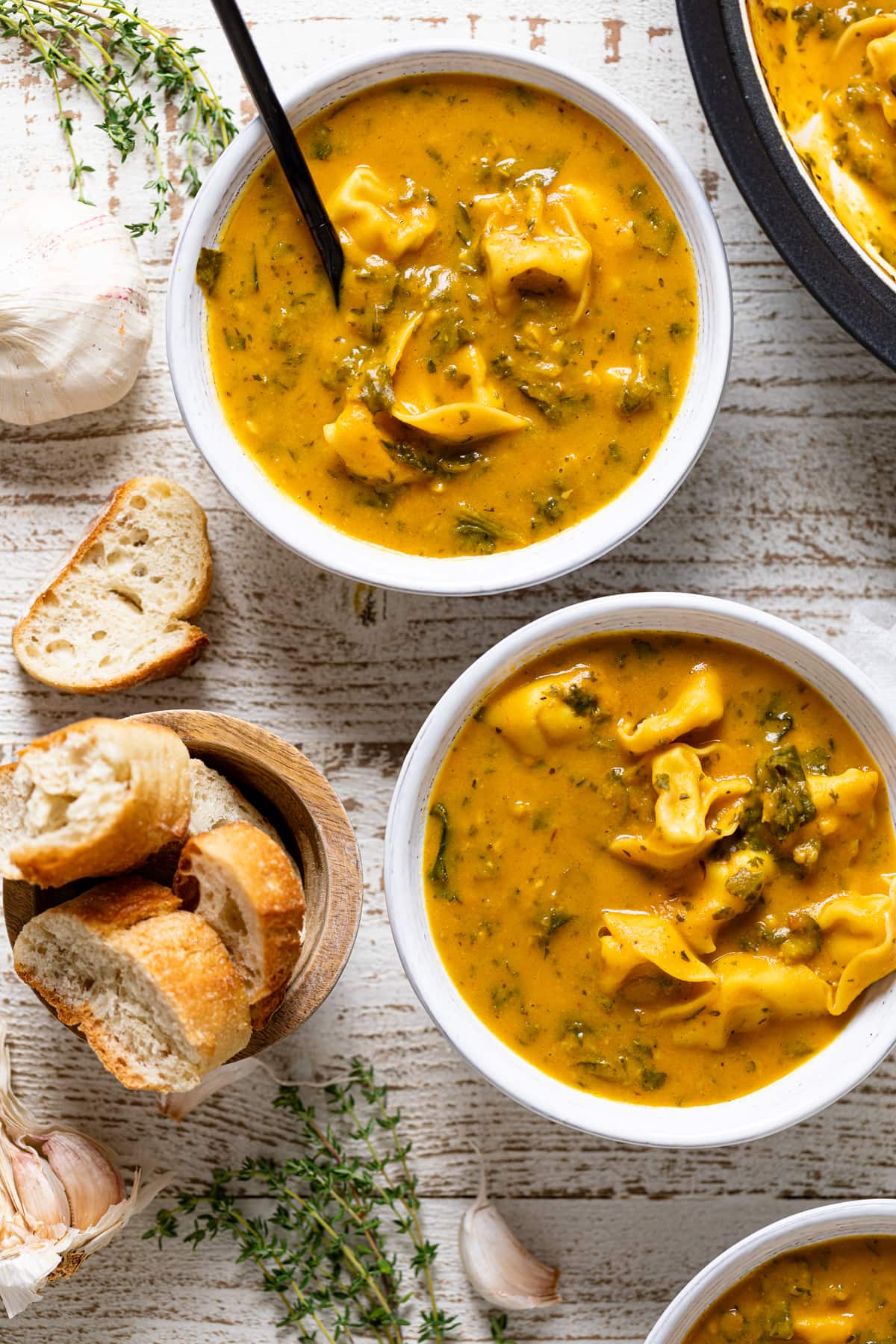 Two bowls of Creamy Cajun Pumpkin Tortellini Soup and a bowl of bread