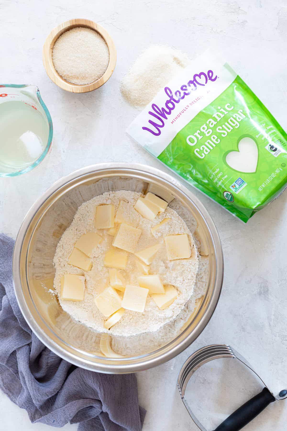 Butter cut into a bowl of dry ingredients next to a bag of Wholesome organic cane sugar.