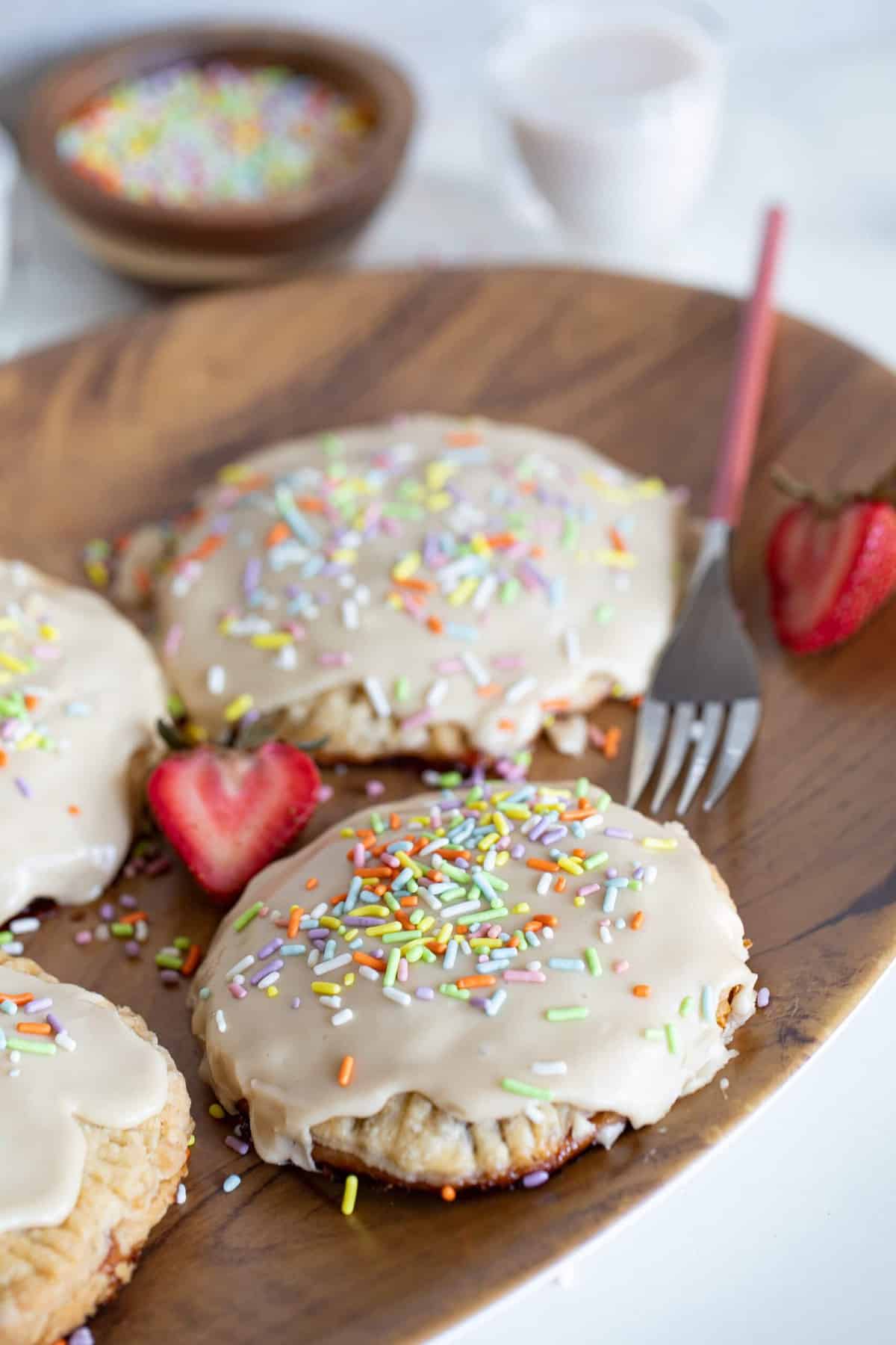 Homemade Vegan Strawberry Pop Tarts topped with sprinkles on a wooden plate.