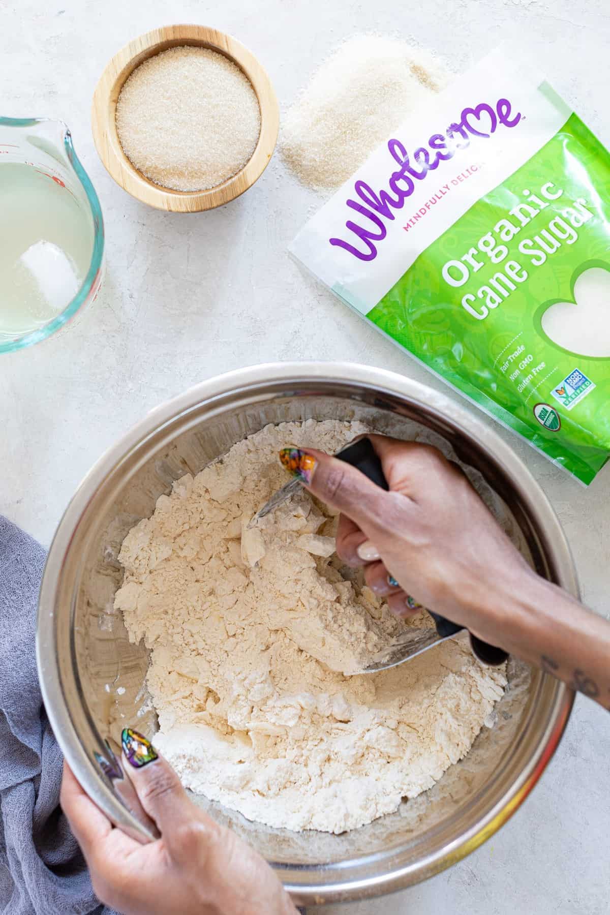 Woman using a pastry blender on a bowl of ingredients next to a bag of Wholesome organic cane sugar.