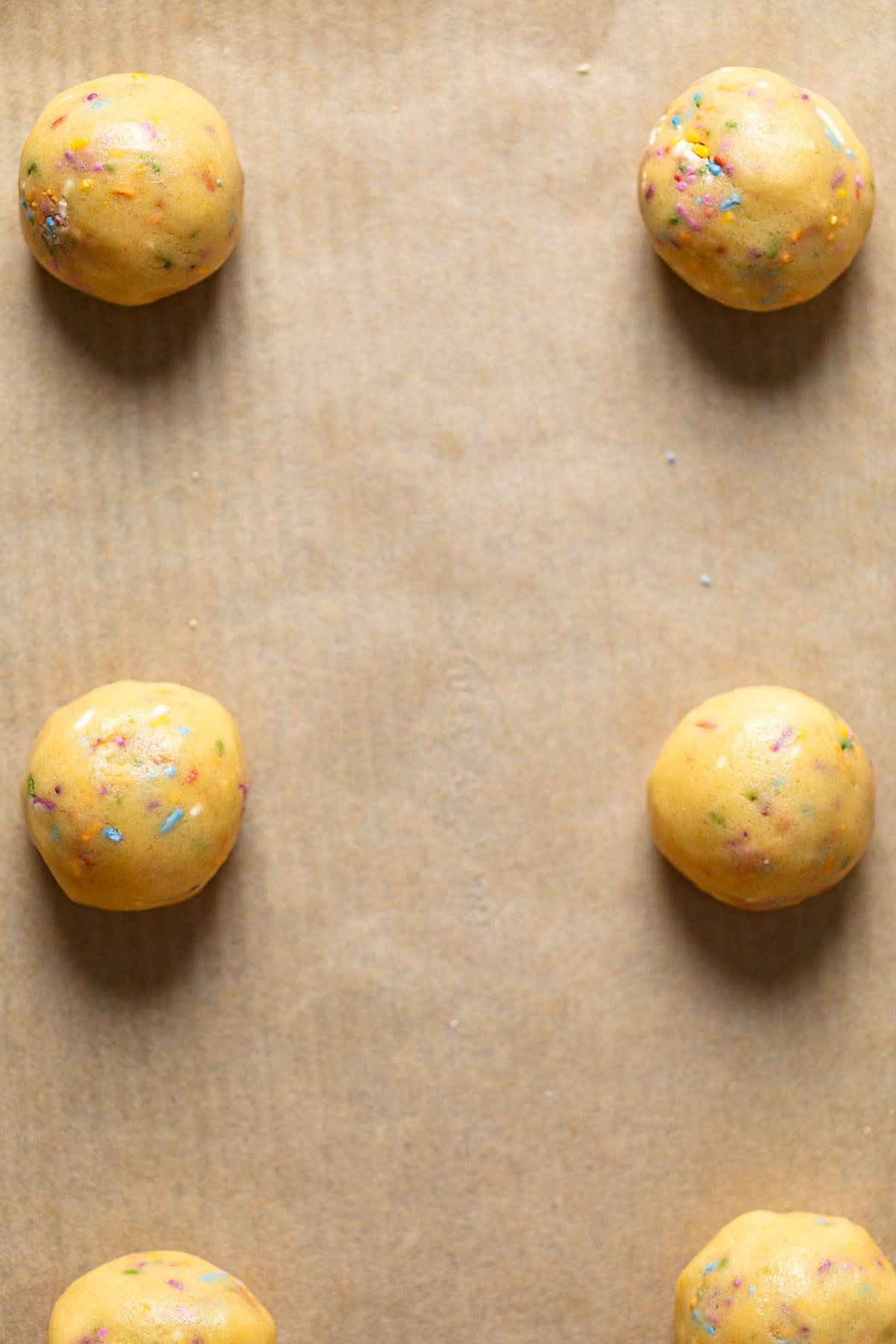 Balls of Sprinkle Sugar Cookies on parchment paper.