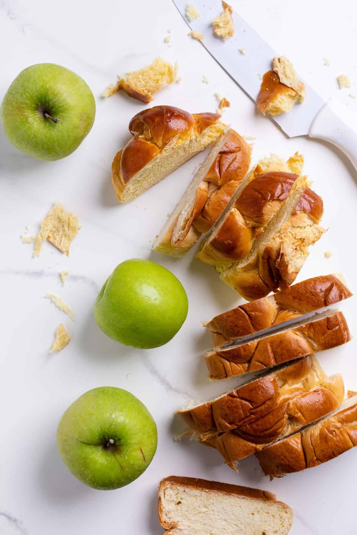 Overhead of slices of challah bread and green apples on a marble counter.