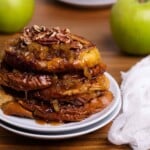 Caramelized Apple French Toast slices on two white plates with a green apple on the side.