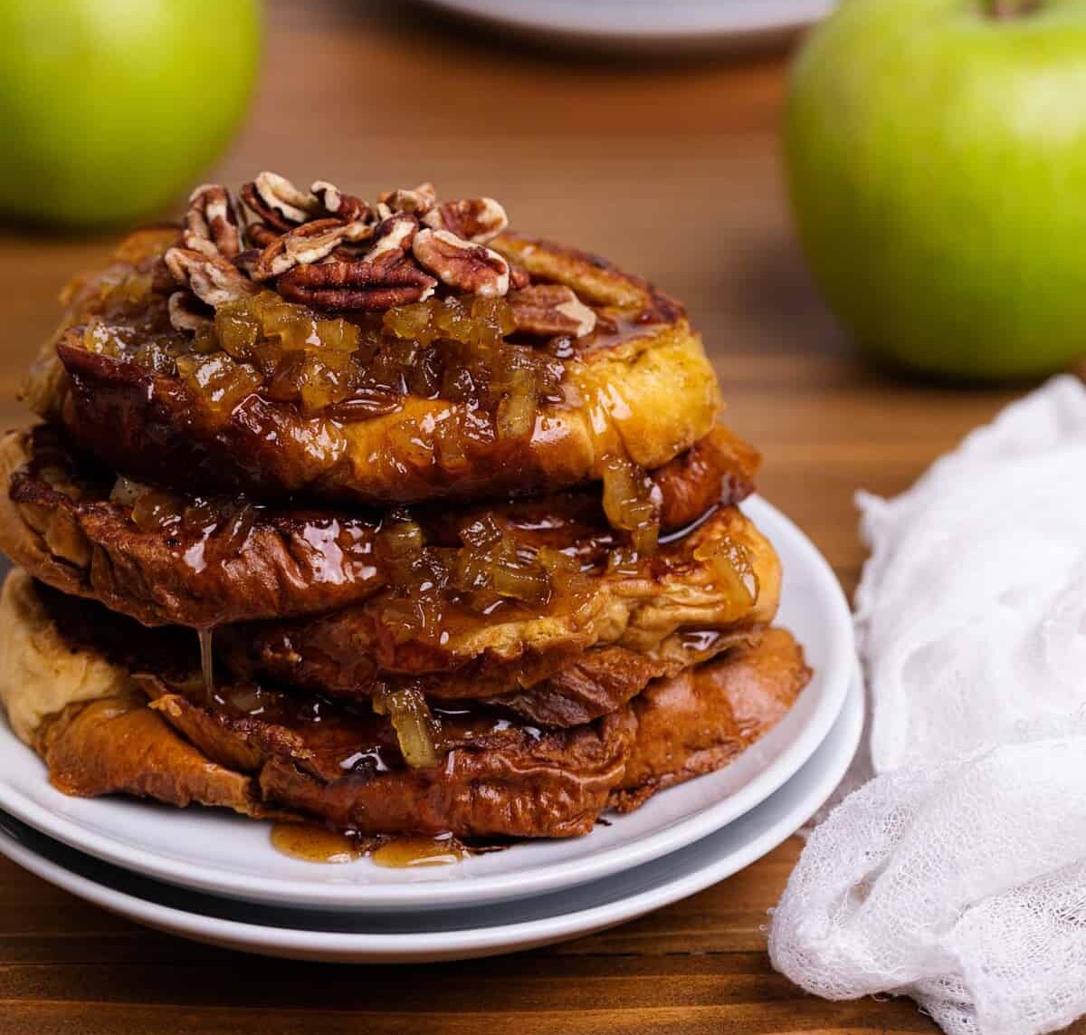 Caramelized Apple French Toast slices on two white plates with a green apple on the side.