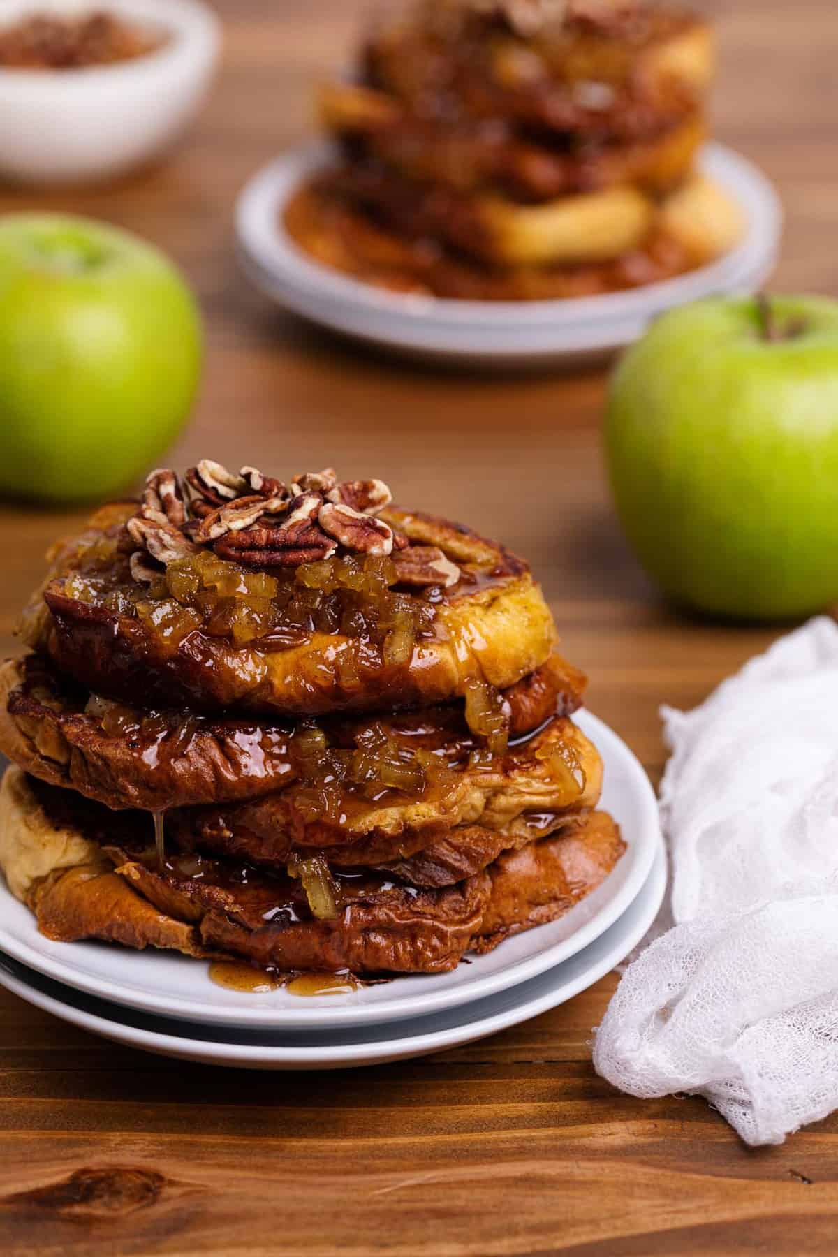 Caramelized Apple French Toast slices on two white plates with a green apple on the side.