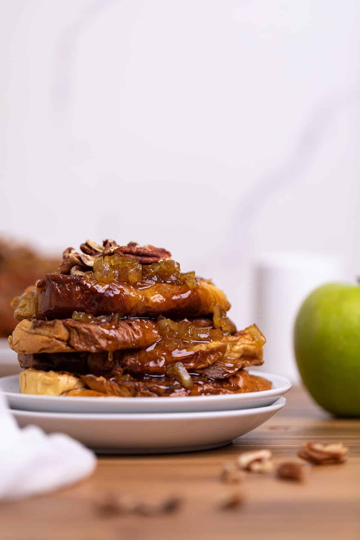 Caramelized Apple French Toast slices on two white plates with a green apple on the side.