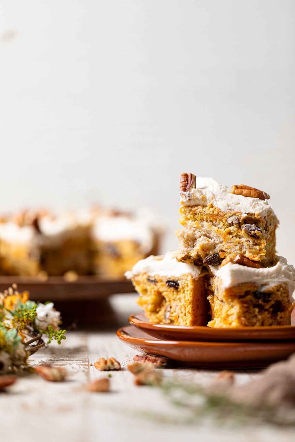 Pieces of Vegan Carrot Cake with Orange-infused Frosting on two small, stacked plates