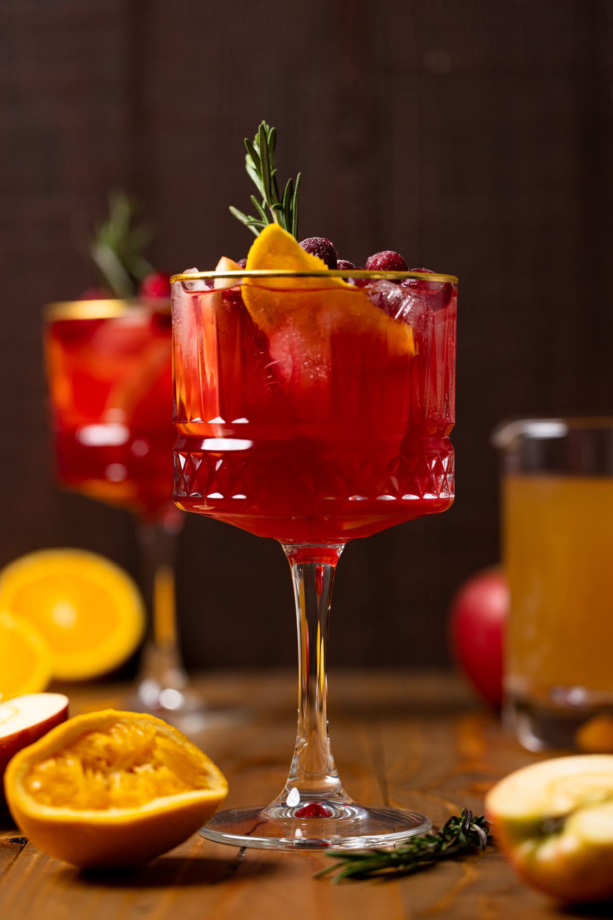 Long-stemmed glass of Cranberry Apple Cider Orange Sangria topped with fruit and a sprig of rosemary