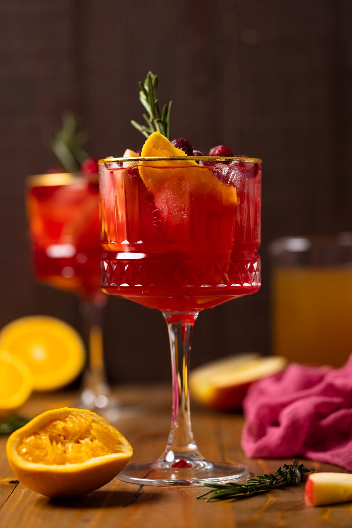 Long-stemmed glass of Cranberry Apple Cider Orange Sangria topped with fruit and a sprig of rosemary