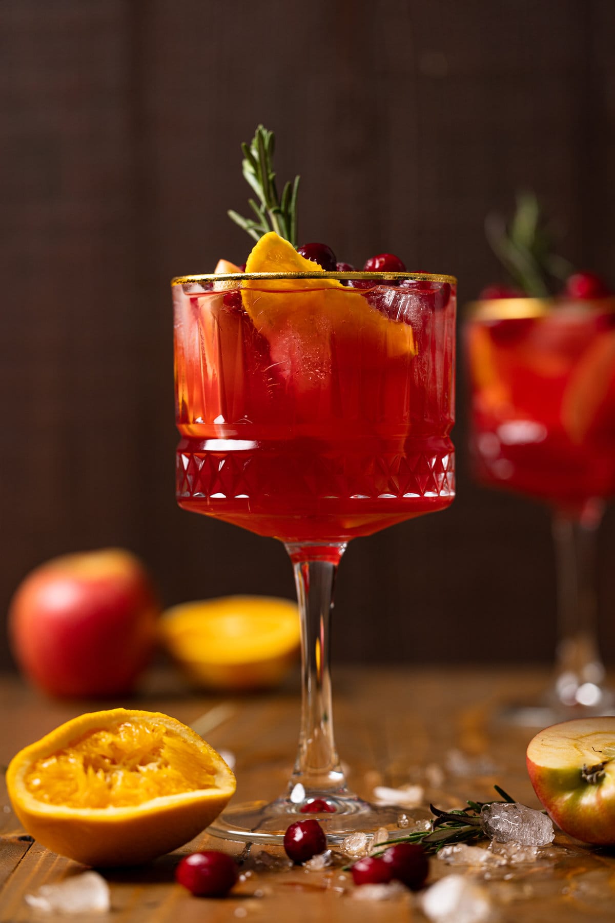 Long-stemmed glass of Cranberry Apple Cider Orange Sangria topped with fruit and a sprig of rosemary on a wooden table