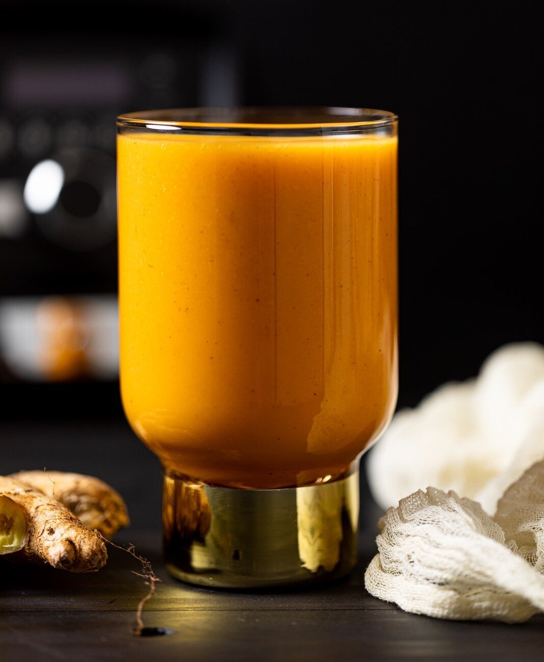 Vegan Jamaican Carrot Juice in a small glass with a golden base on a table with ginger