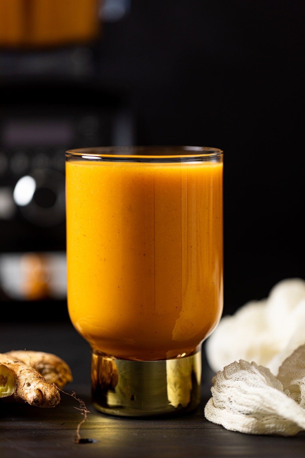 Vegan Jamaican Carrot Juice in a small glass with a golden base on a table with ginger