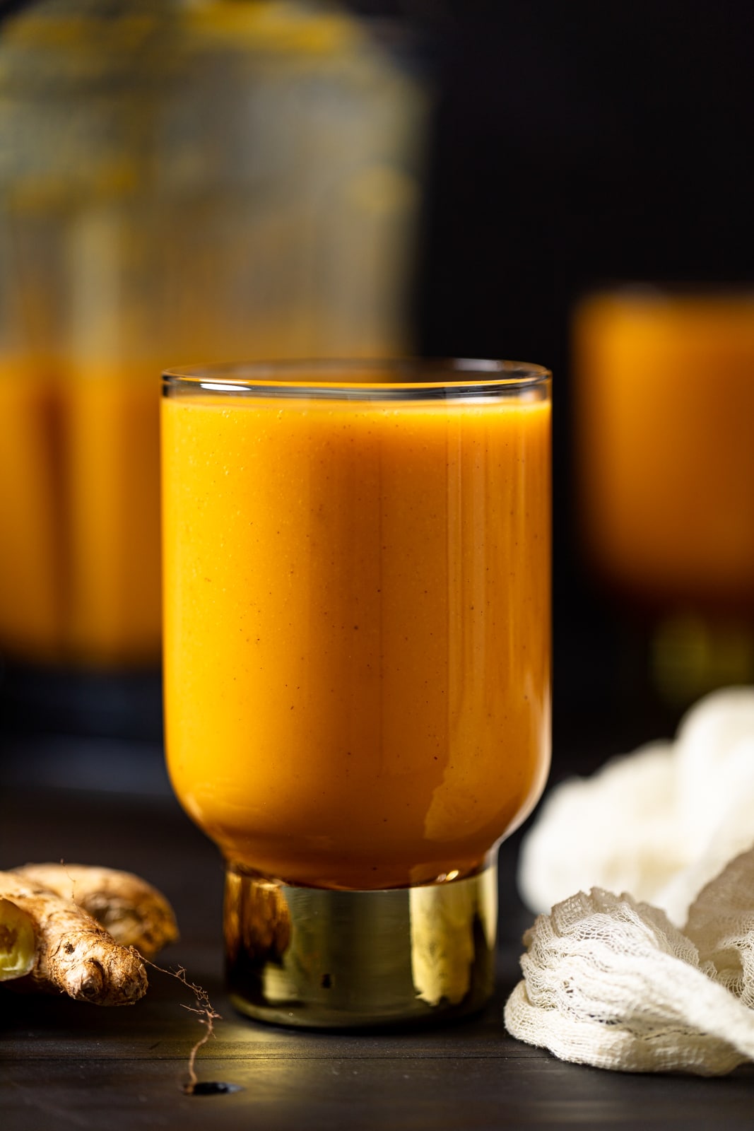 Vegan Jamaican Carrot Juice in a small glass with a golden base on a table with ginger