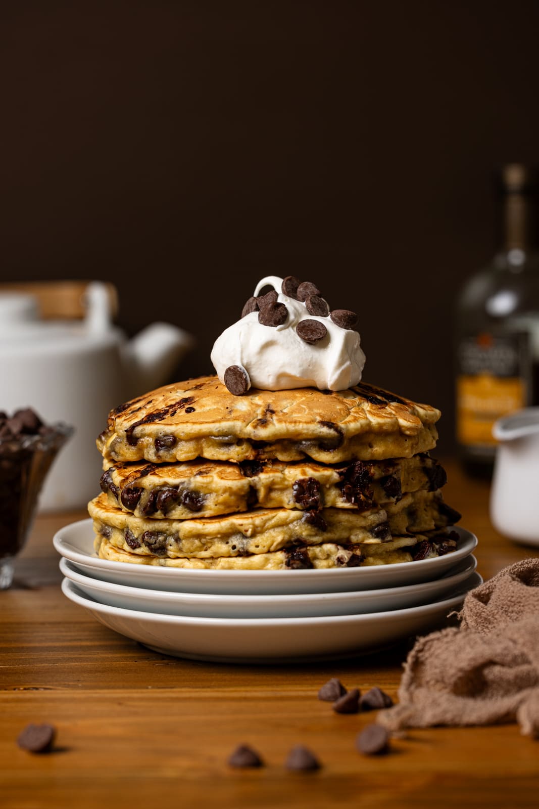 Stack of pancakes on white plates with chocolate chips and whipped cream.