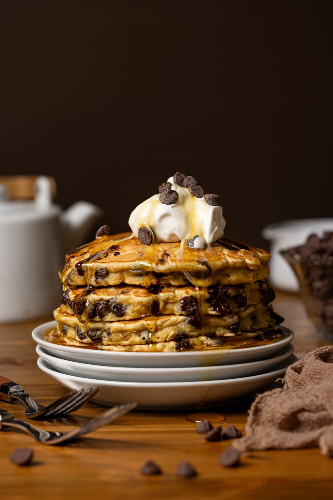 Stack of chocolate chip pancakes with syrup, whipped cream, and fork.