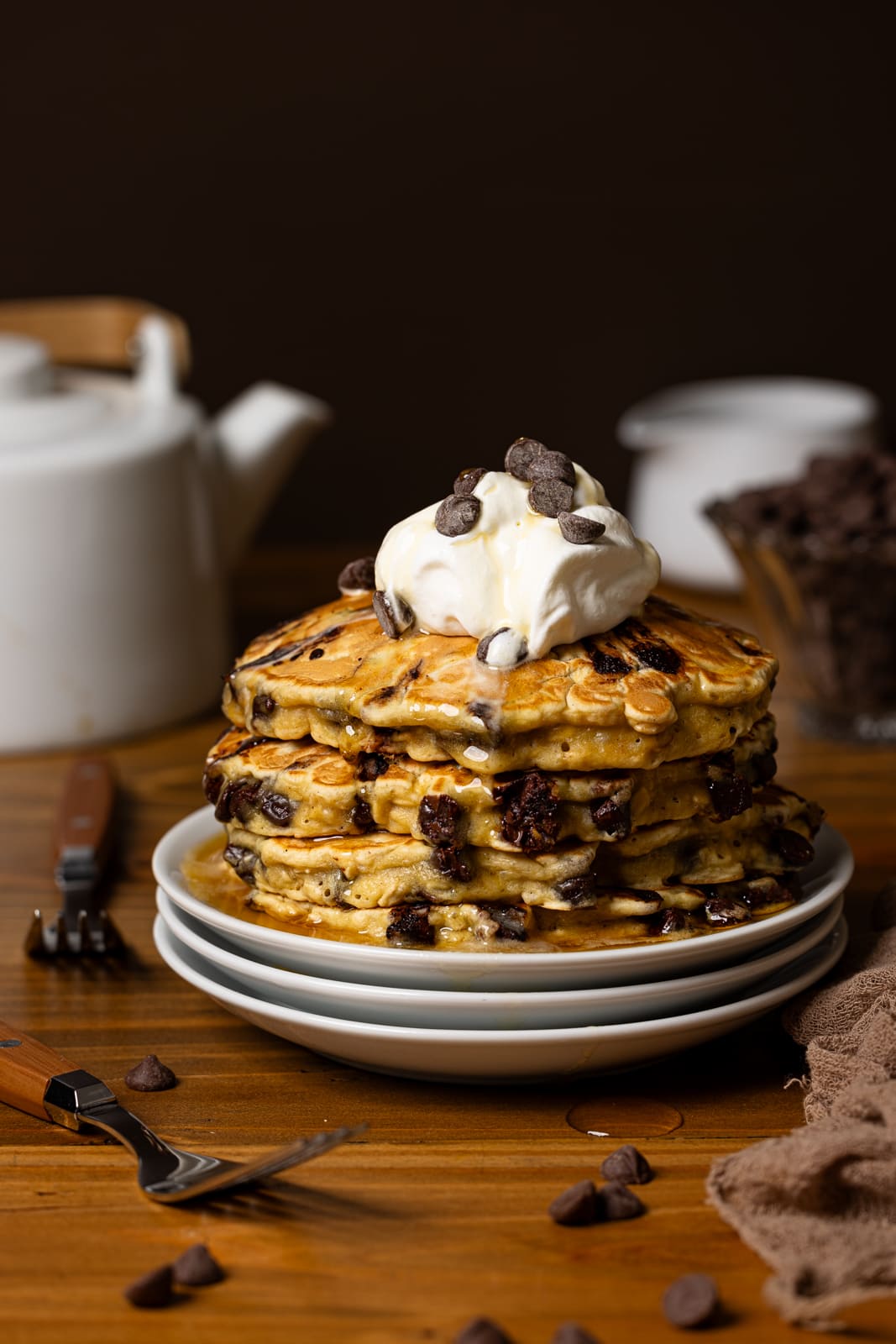 Stack of pancakes on white plates with a kettle and fork.