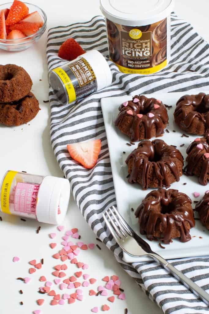 Valentine\'s Day Mini Chocolate Brownie Bundt Cakes with jars of sprinkles and icing.