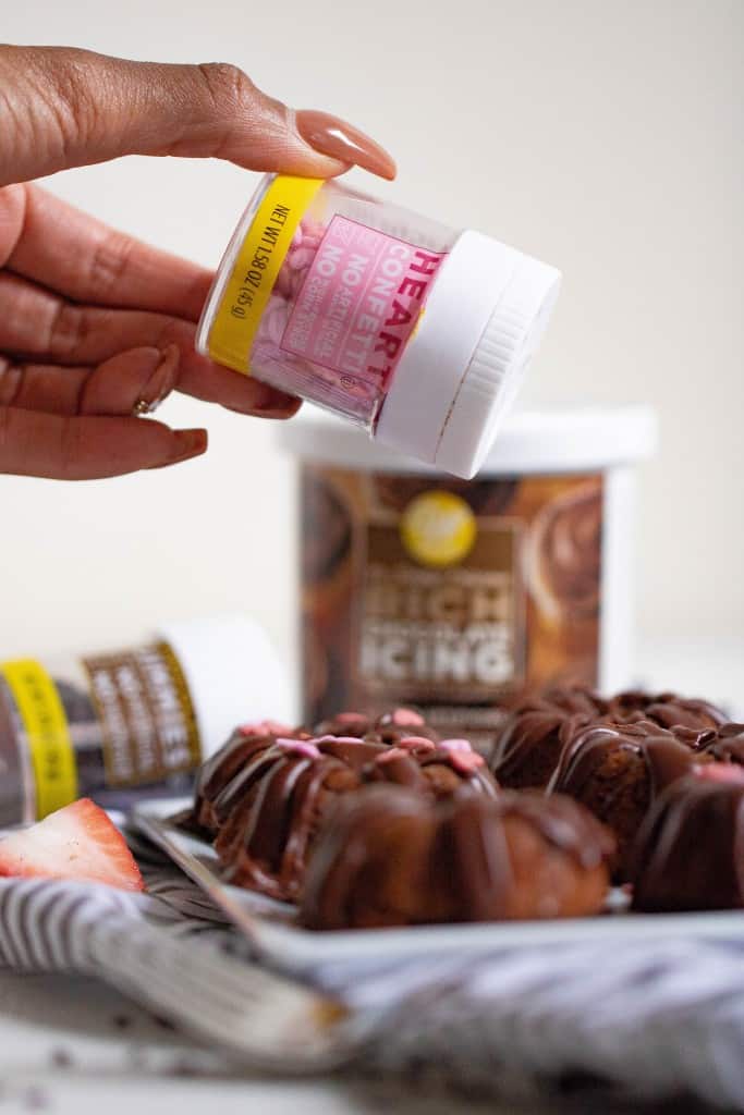 Woman pouring heart sprinkles onto Valentine\'s Day Mini Chocolate Brownie Bundt Cakes.