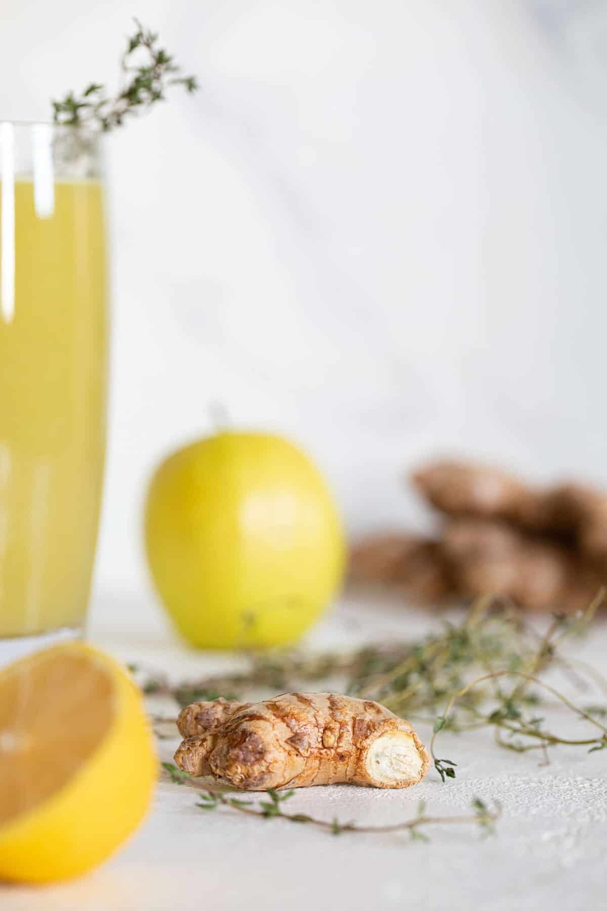 Ginger, lemon, apple, and thyme on a countertop.