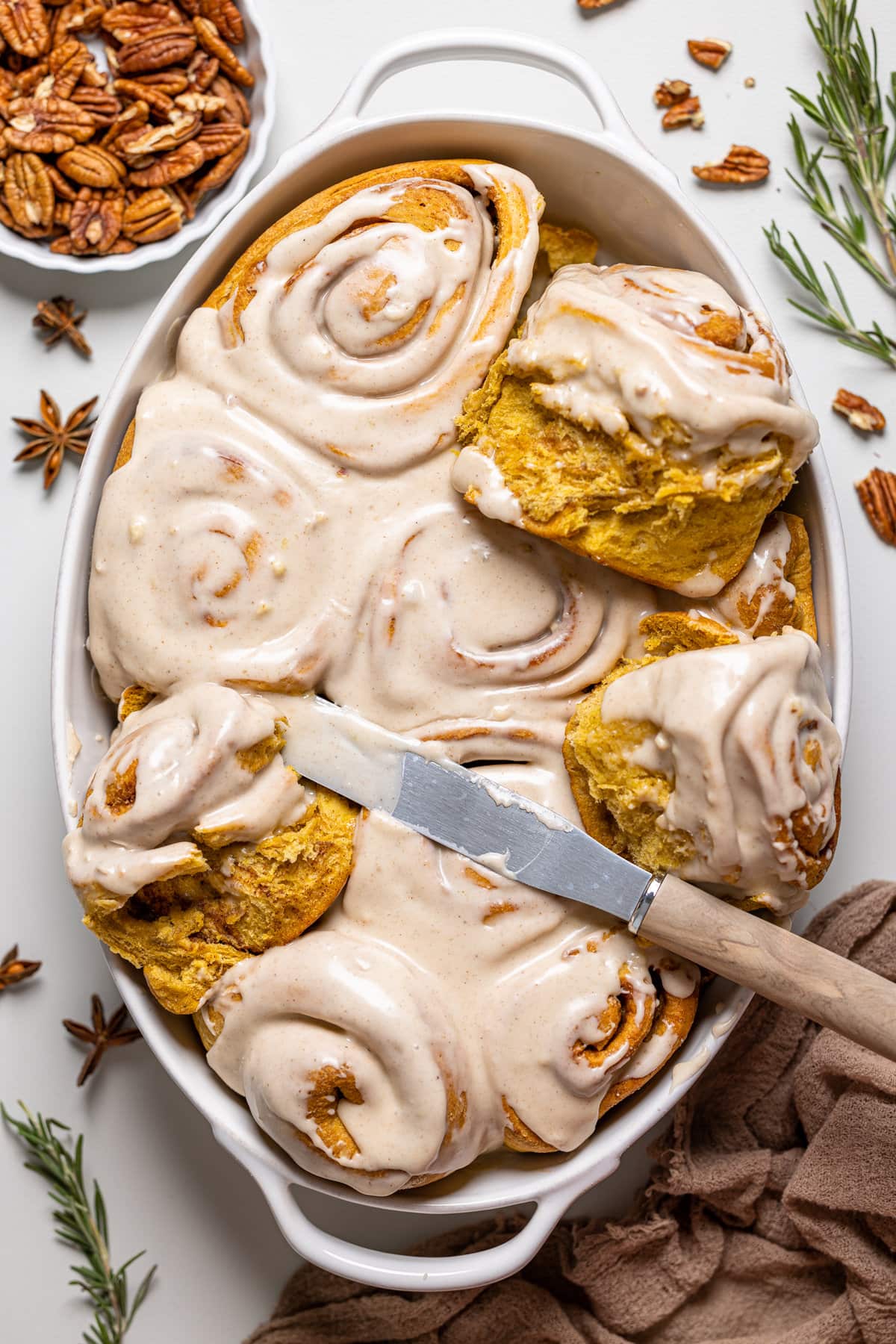 Icing knife spreading glaze on a baking pan of Vegan Sweet Potato Cinnamon Rolls 