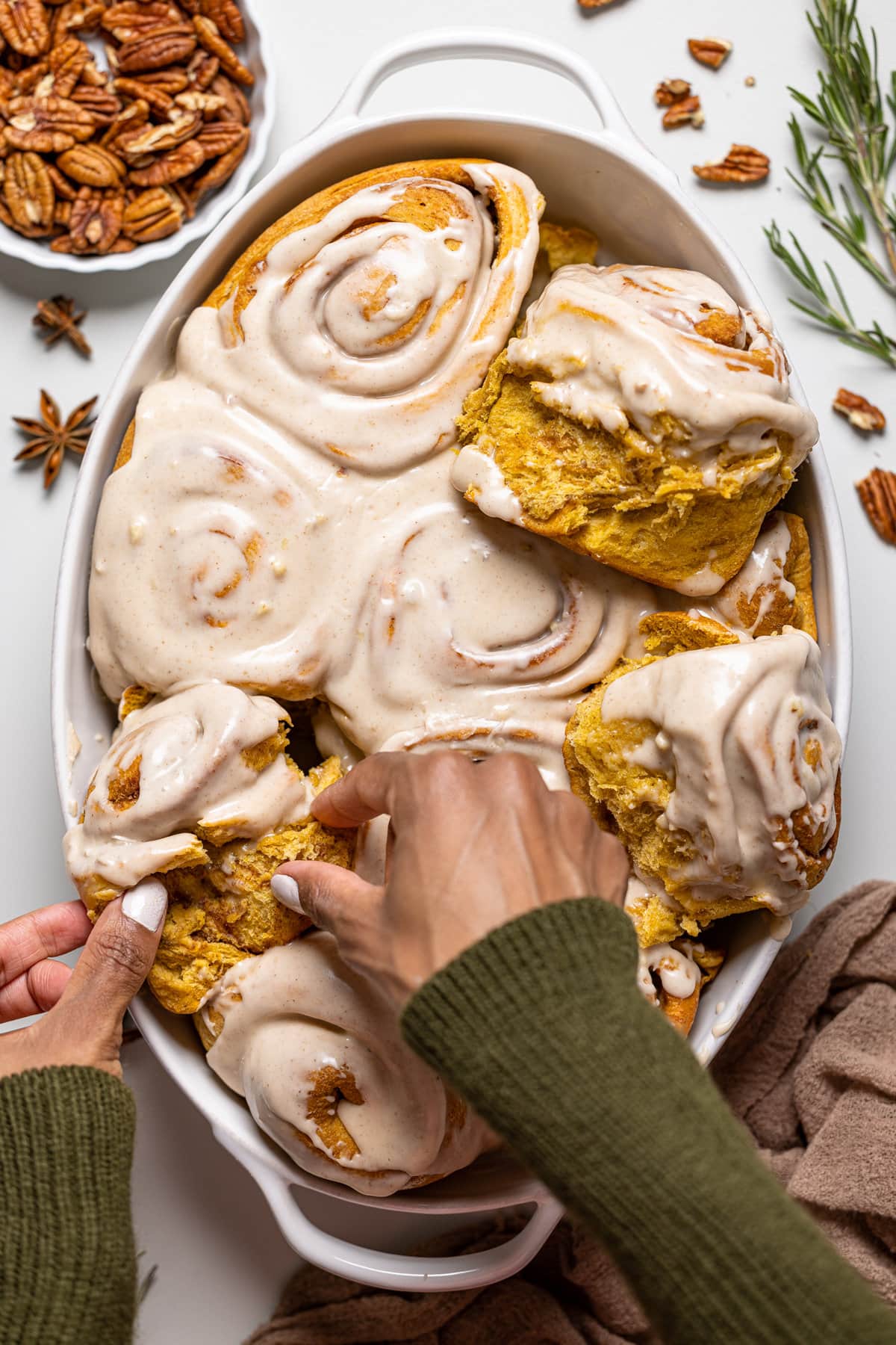 Hands grabbing a Vegan Sweet Potato Cinnamon Roll from a baking pan