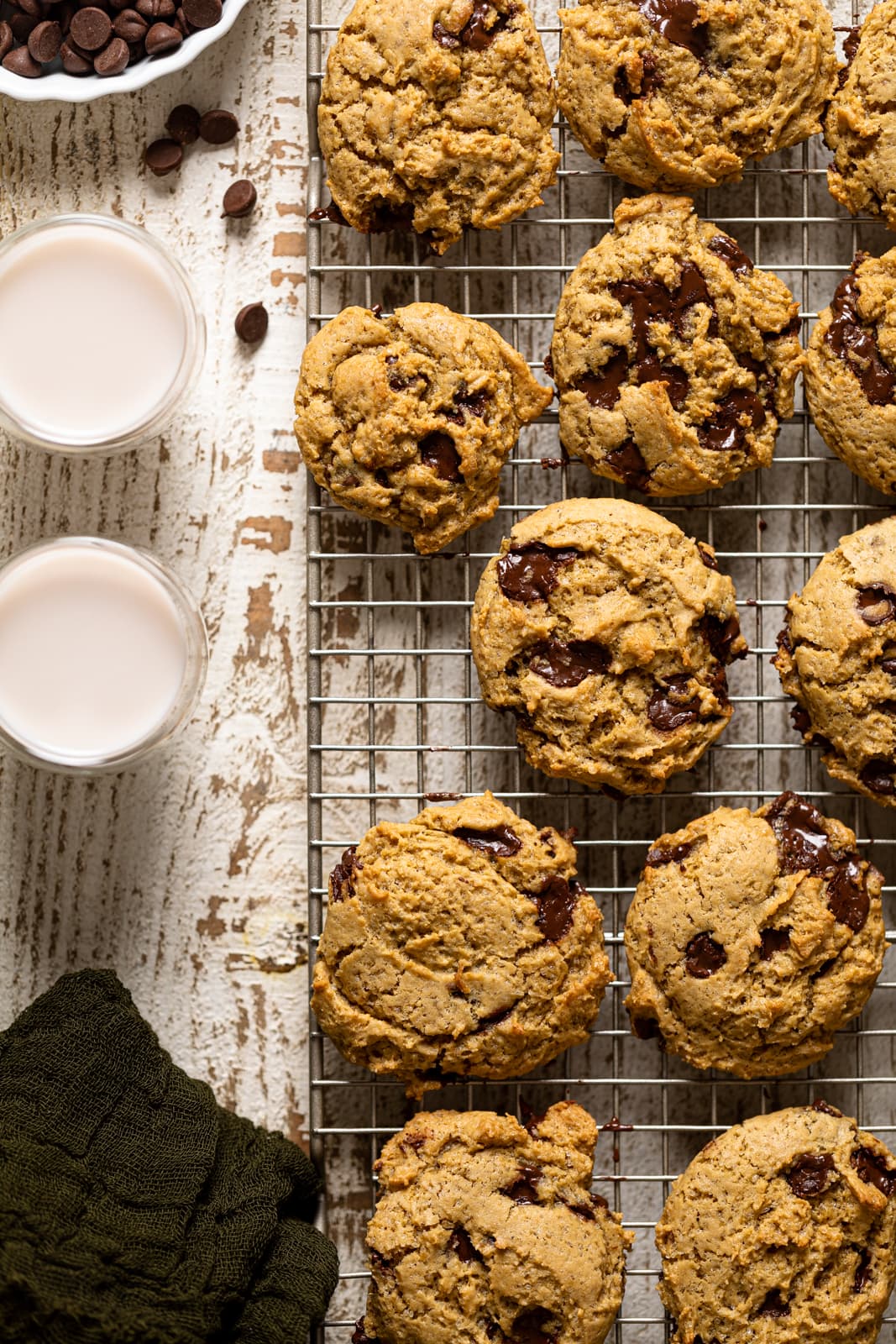 Vegan Chocolate Chip Cookies on a wire rack with glasses of dairy-free milk