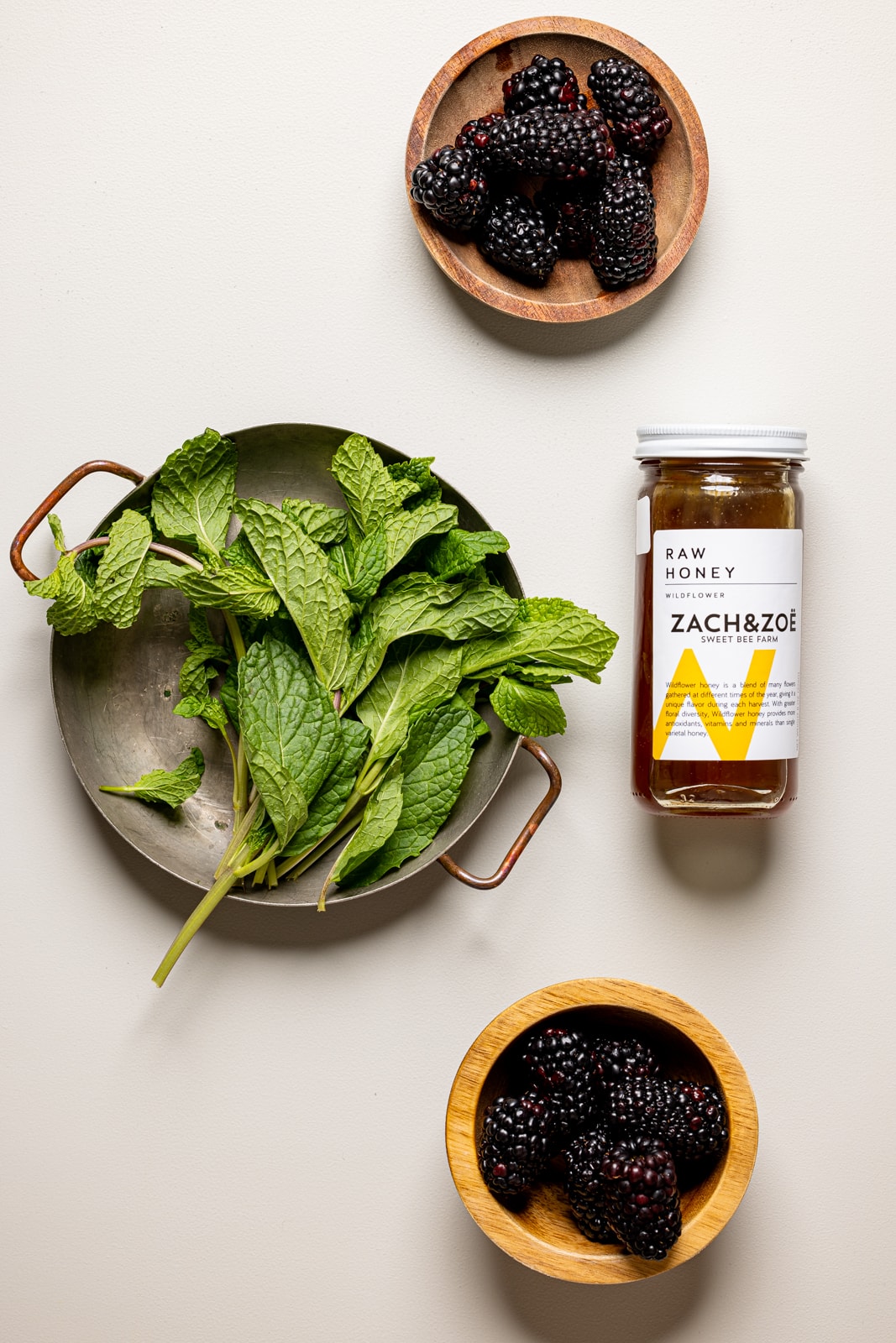 Ingredients on a light grey table including mint leaves, blackberries, and honey.