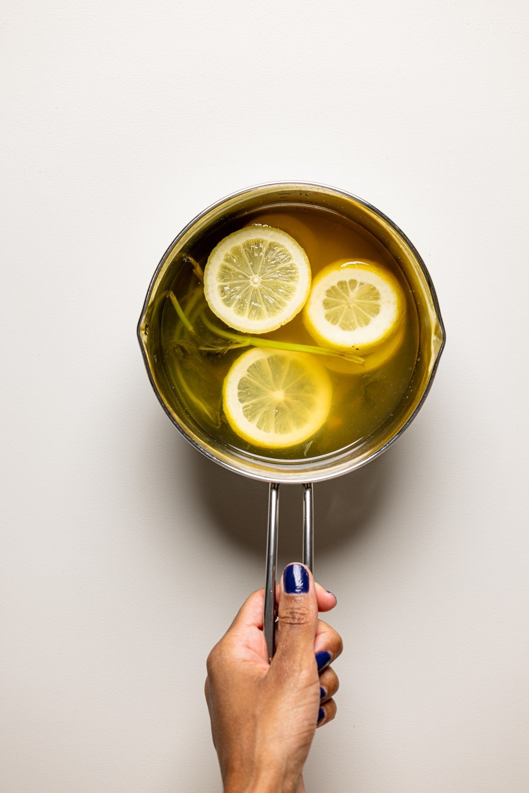 Lemon syrup in a saucepan on a light brown table being held.