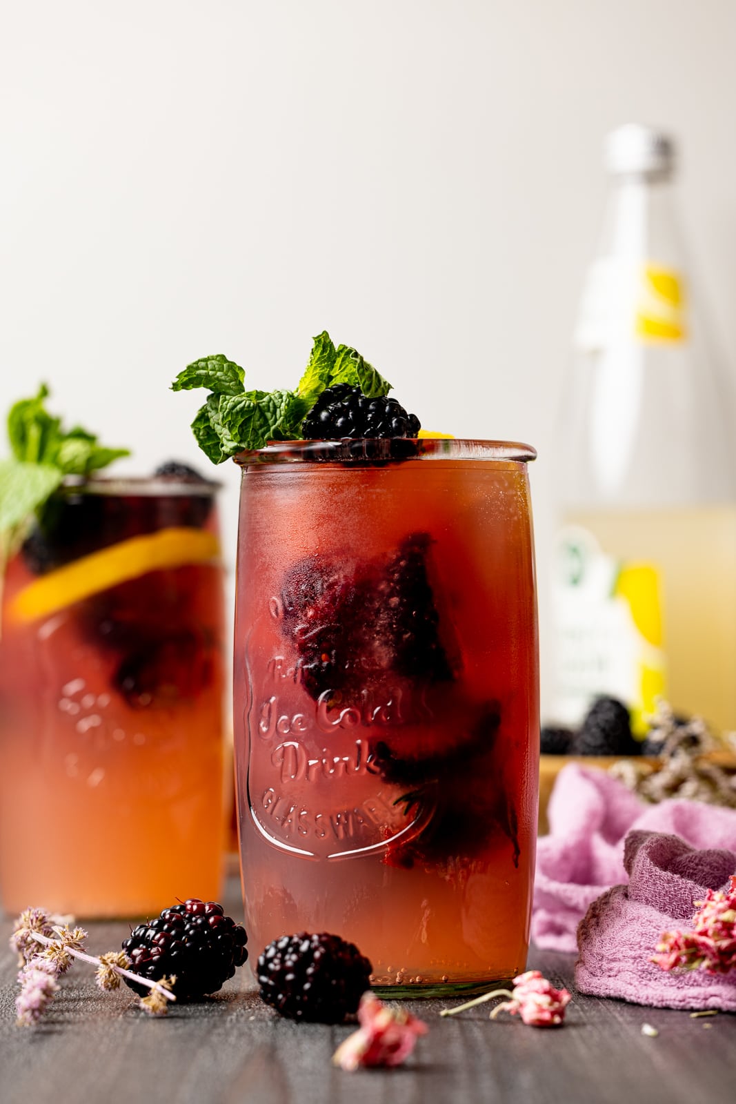 Two jars filled with iced tea on a grey wood table with blackberries.