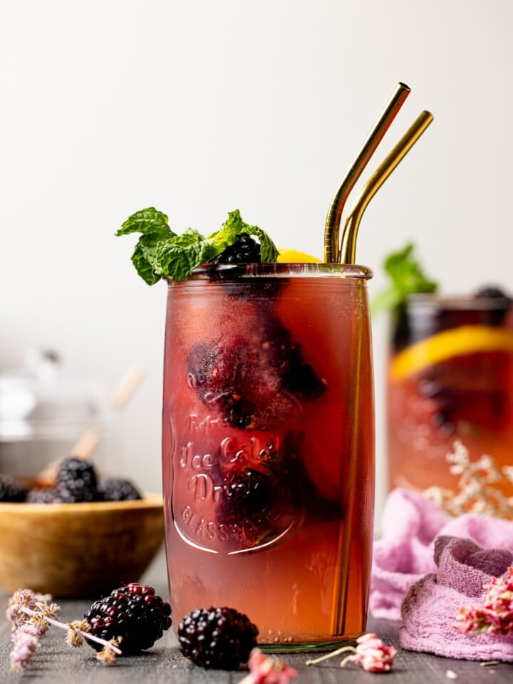 Iced tea in a jar with two gold straws with blackberries and mint leaves.