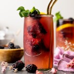 Iced tea in a jar with two gold straws with blackberries and mint leaves.