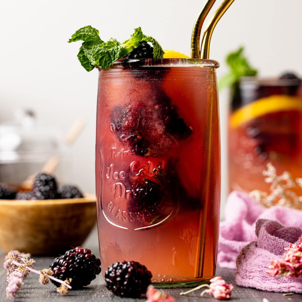 Iced tea in a jar with two gold straws with blackberries and mint leaves.