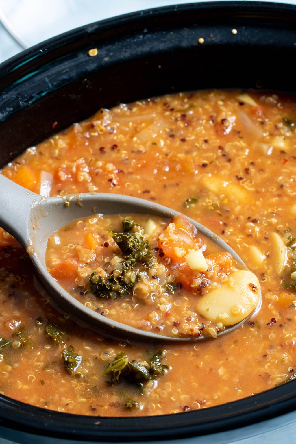 Spoon scooping Quinoa Veggie Soup from a Slow Cooker.