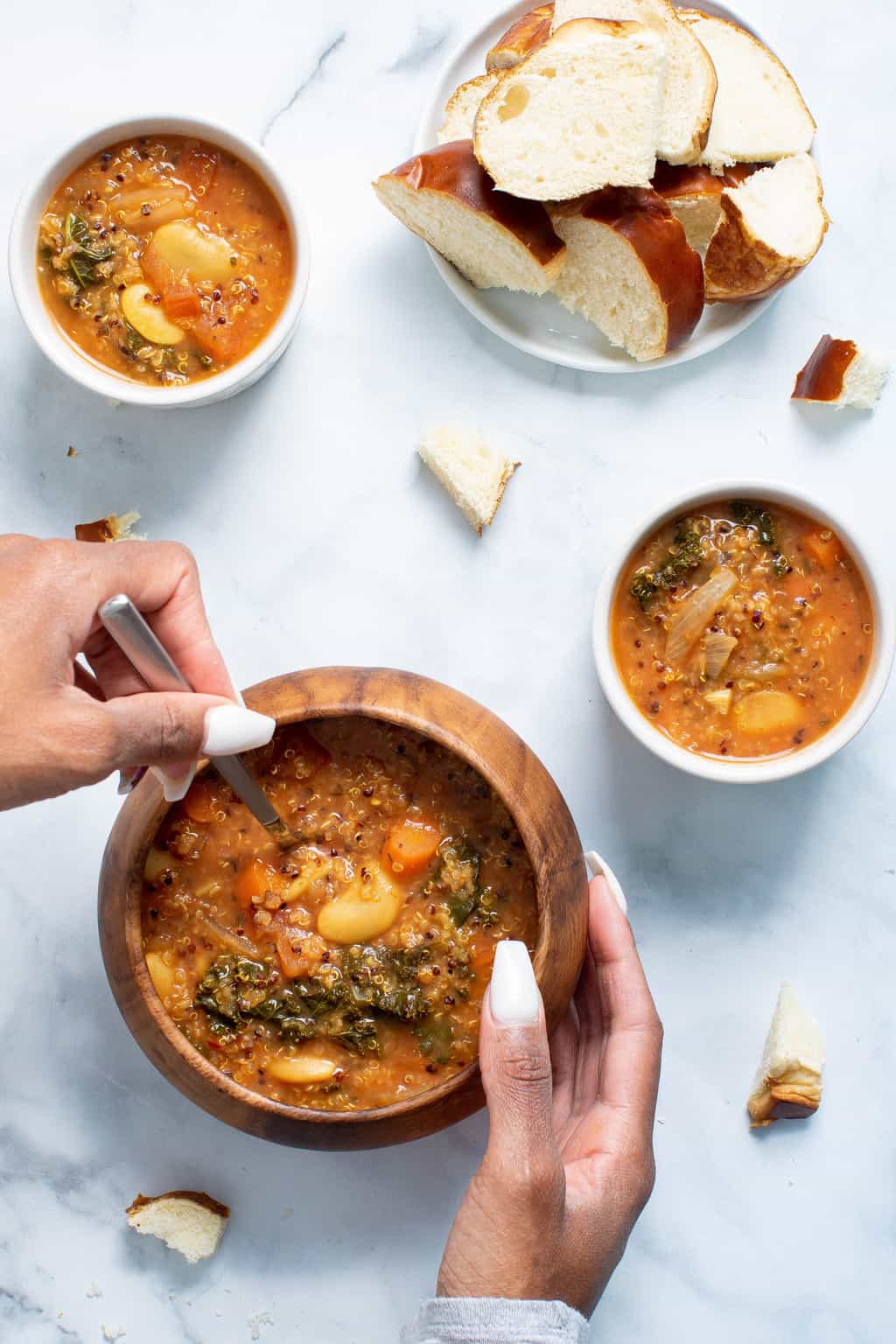 Woman using a spoon to scoop Quinoa Veggie Soup from a wooden bowl.