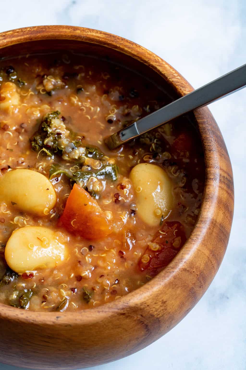 Spoon in a wooden bowl of Quinoa Veggie Soup.