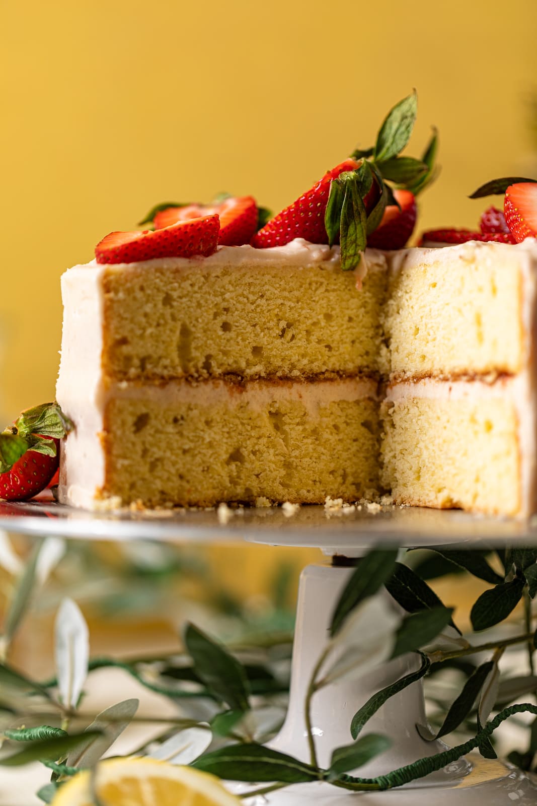 Elevated platter with a Lemon Strawberry Layer Cake that is missing a slice