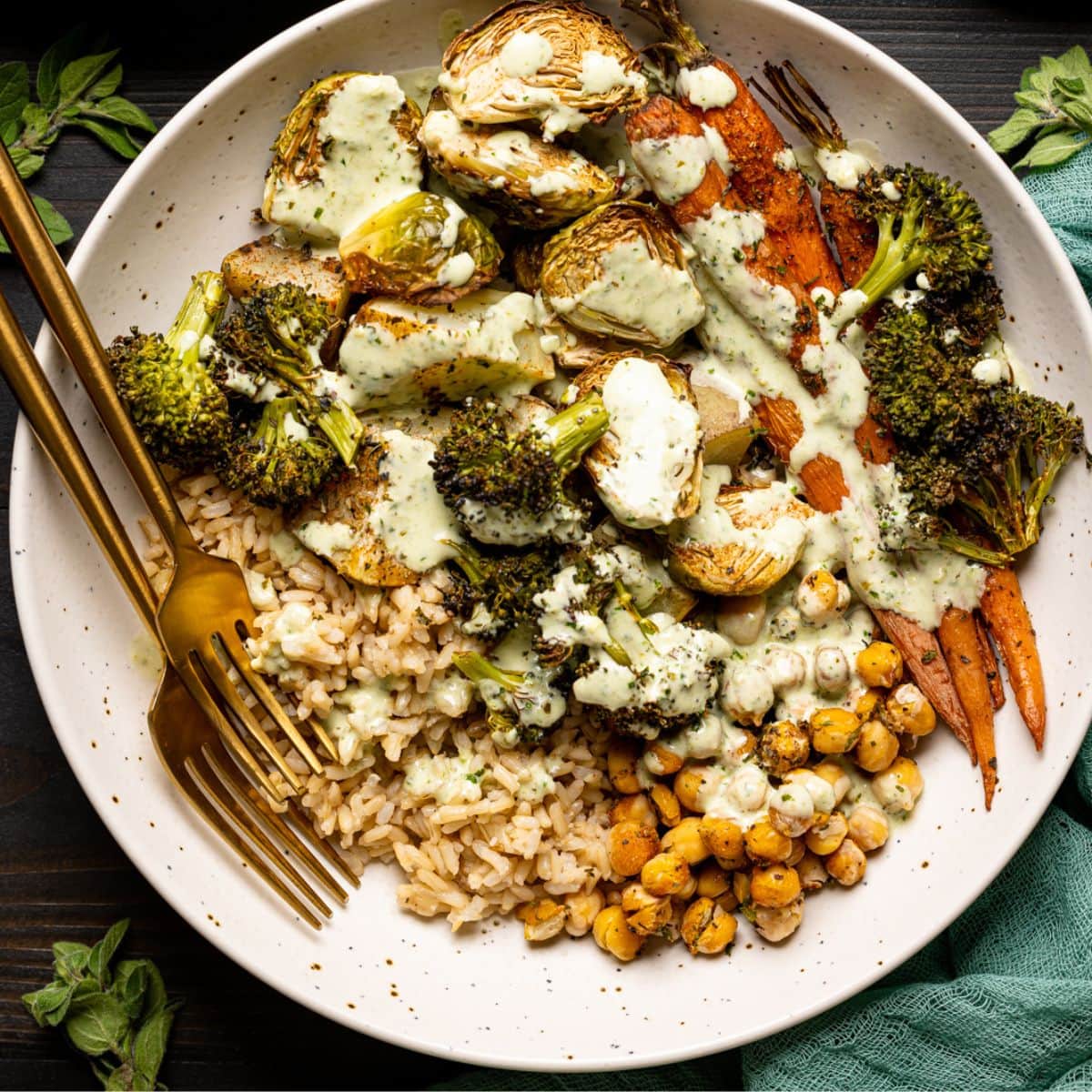 Veggie bowl in two low bowls on a black table with pesto sauce and two forks and herbs.