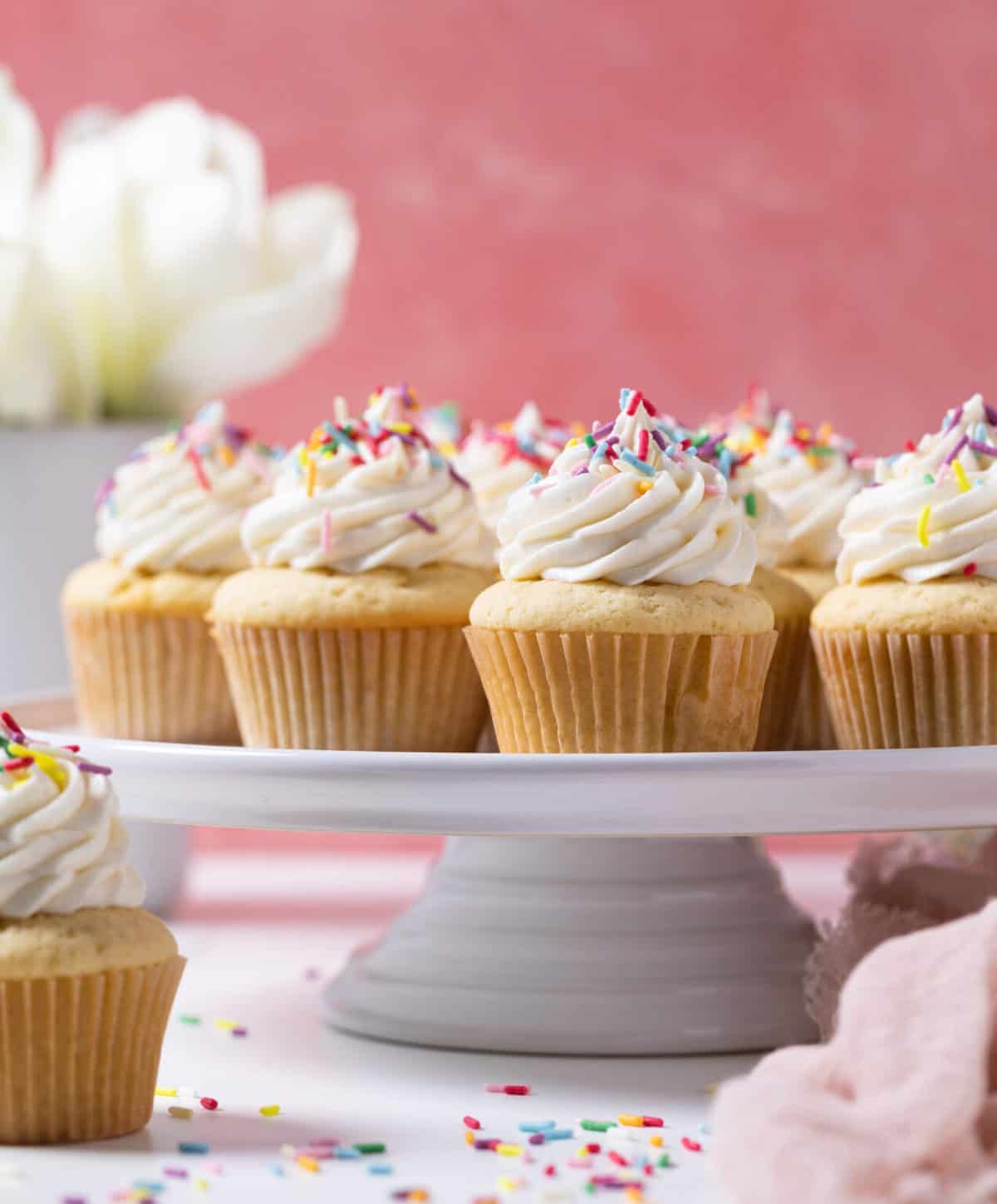 Vanilla Cupcakes with Buttercream Frosting topped with sprinkles on an elevated platter.