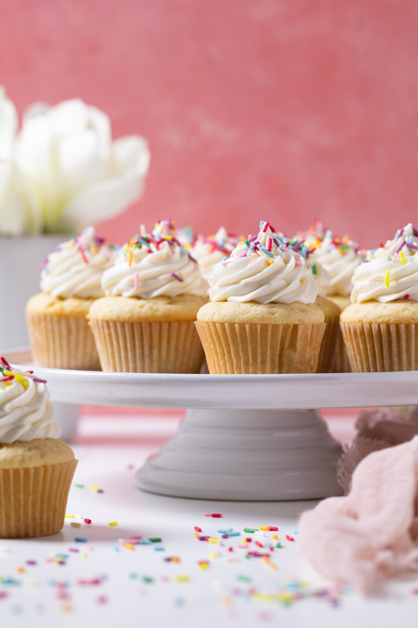 Vanilla Cupcakes with Buttercream Frosting topped with sprinkles on an elevated platter.